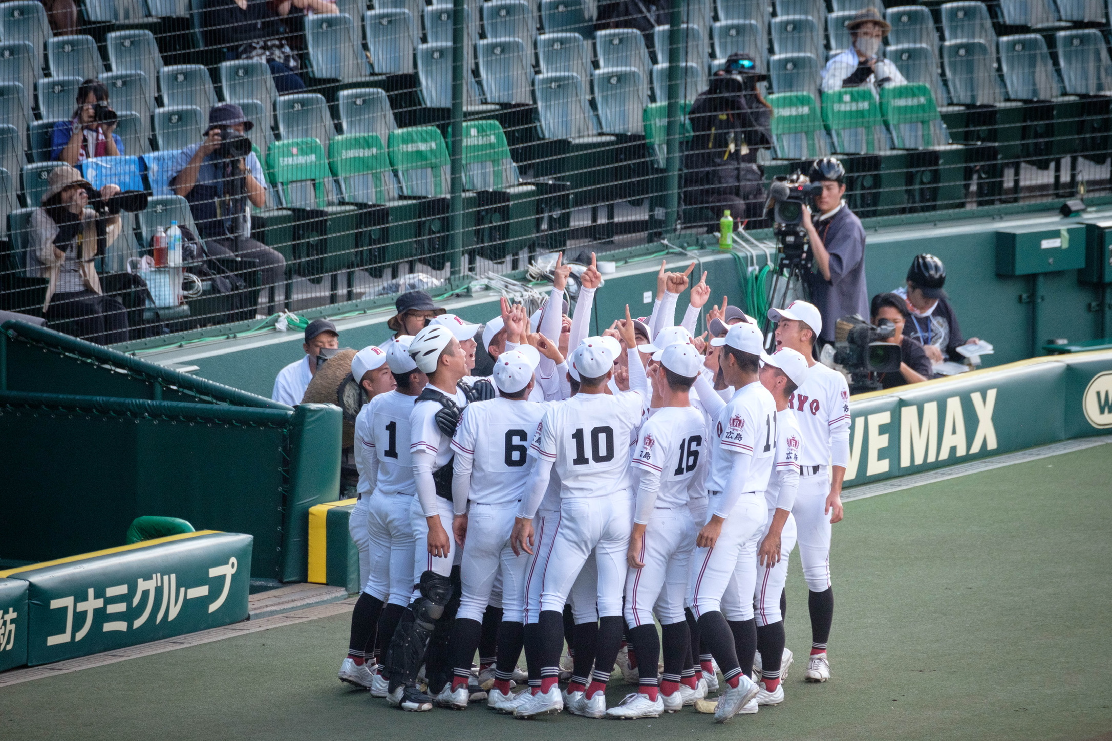 A baseball team raising their hands together beside the field
