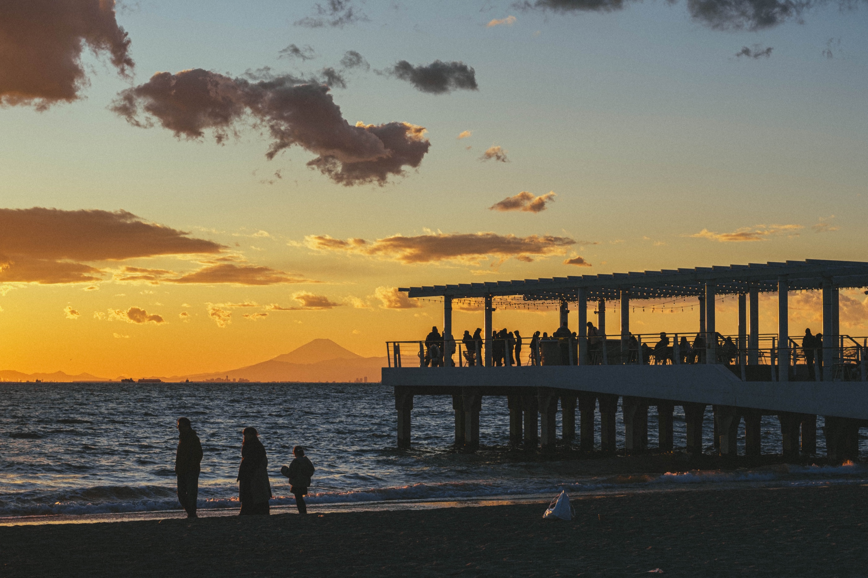 People gathered on a pier at sunset with a mountain on the horizon