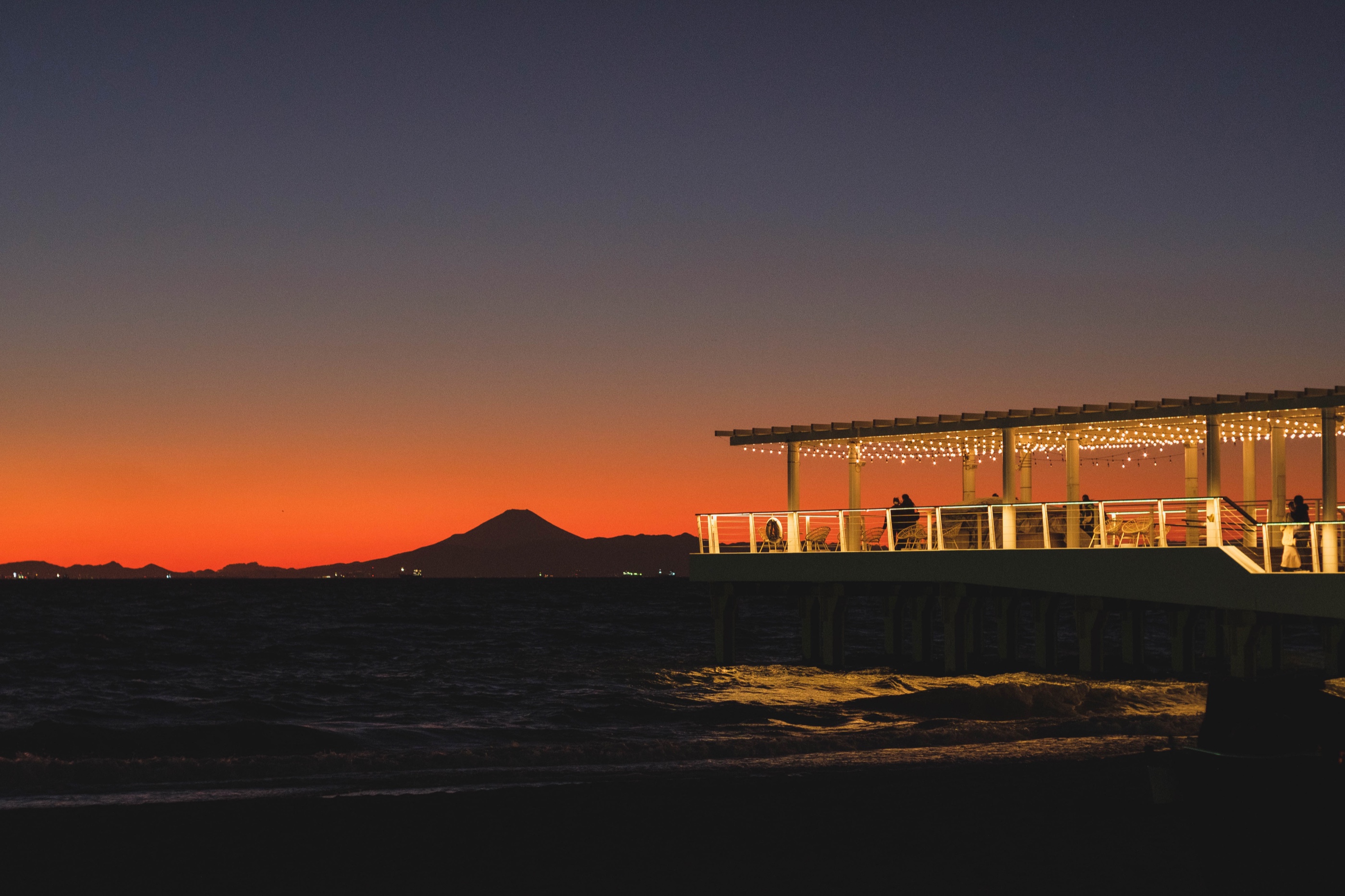 An illuminated pier and mountain silhouette after sunset