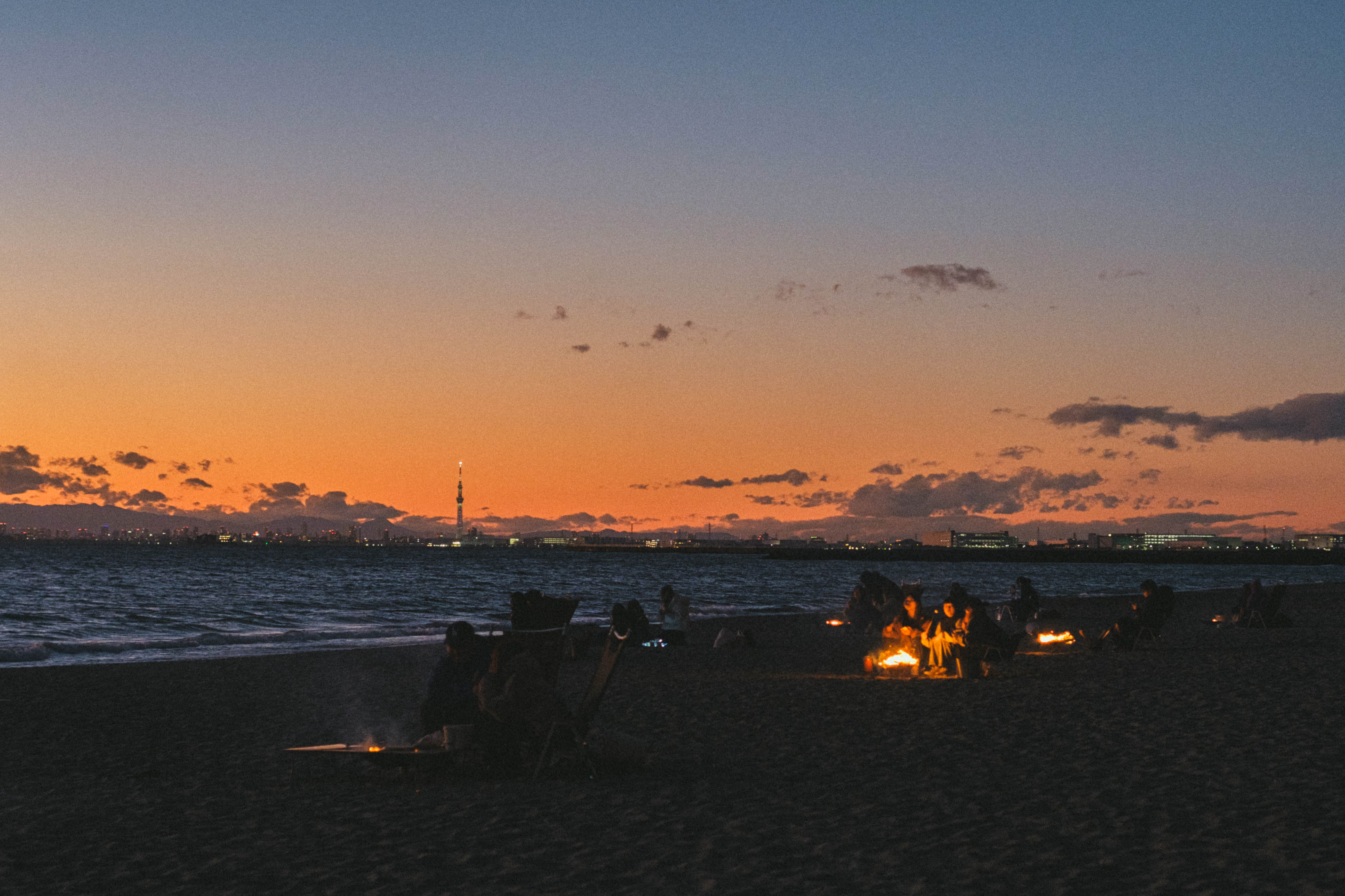 Small bonfires glowing on a beach beneath an orange skyline