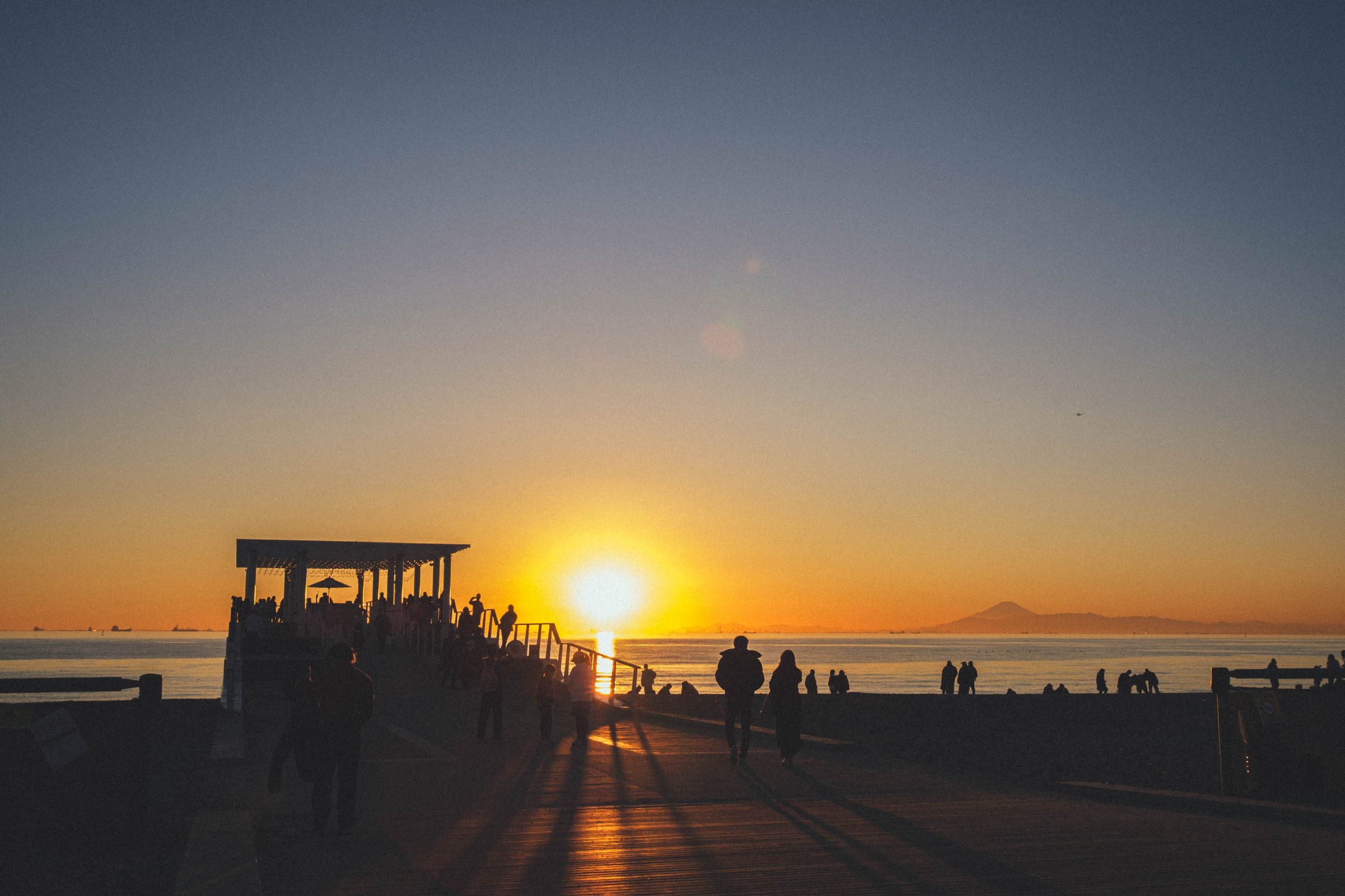 People casting long shadows beside a pier at sunset