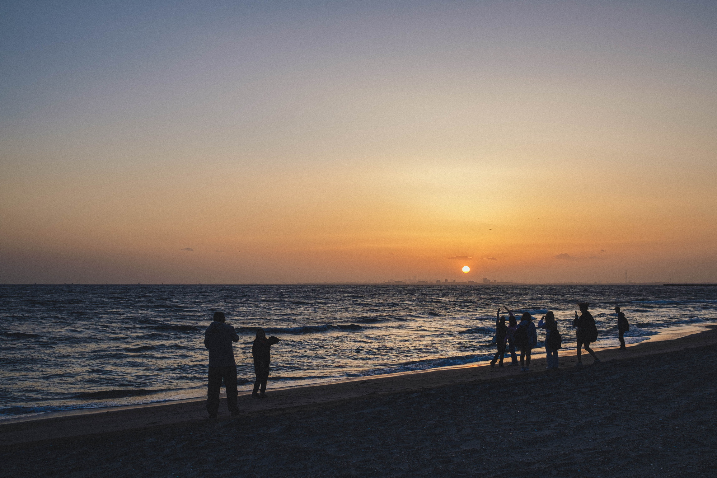 People gathered at the water's edge as the sun sets